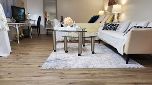 A modern living room with a glass coffee table, a sofa, and a TV on a wooden floor.