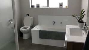 A modern bathroom with a toilet, bathtub, and sink. - Land escape in Bream Bay (Waipu)