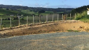 A rural landscape with rolling hills, a gravel road, and a fence. - Land escape in Bream Bay (Waipu)