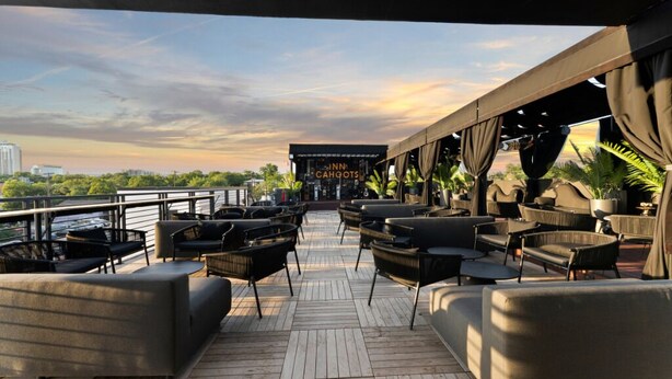 Une terrasse avec des sièges extérieurs, une enseigne indiquant « Inn Cahoots », et une vue sur les gratte-ciel de la ville.