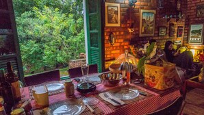 A dining table set with plates, cutlery, and a bottle, surrounded by chairs, with a view of greenery outside.