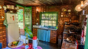 A rustic kitchen with a brick wall, wooden ceiling, and a green door.