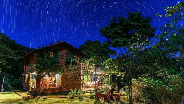A brick house with a porch and a garden, under a starry night sky.