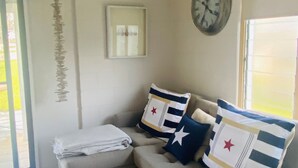 A living room with a beige sofa, two pillows with star designs, a round woven rug, a wall clock, and a framed picture. - THE SHACK - GOOLWA CENTRAL (Goolwa)