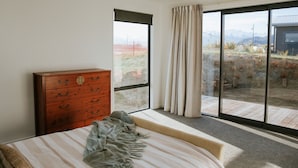 Una camera da letto con un'ampia finestra, un comò in legno, un letto con copripiumino a righe e vista su un paesaggio montuoso.