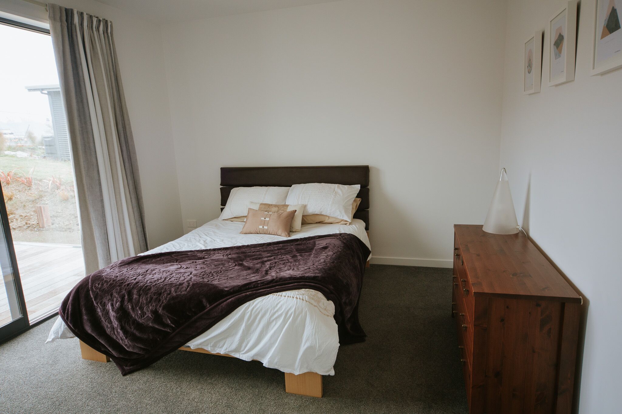 A bedroom with a bed, a wooden dresser, and a window with curtains.