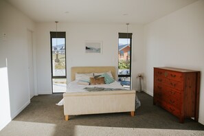 A bedroom with a bed, a dresser, and a window with a view of a house and mountains.