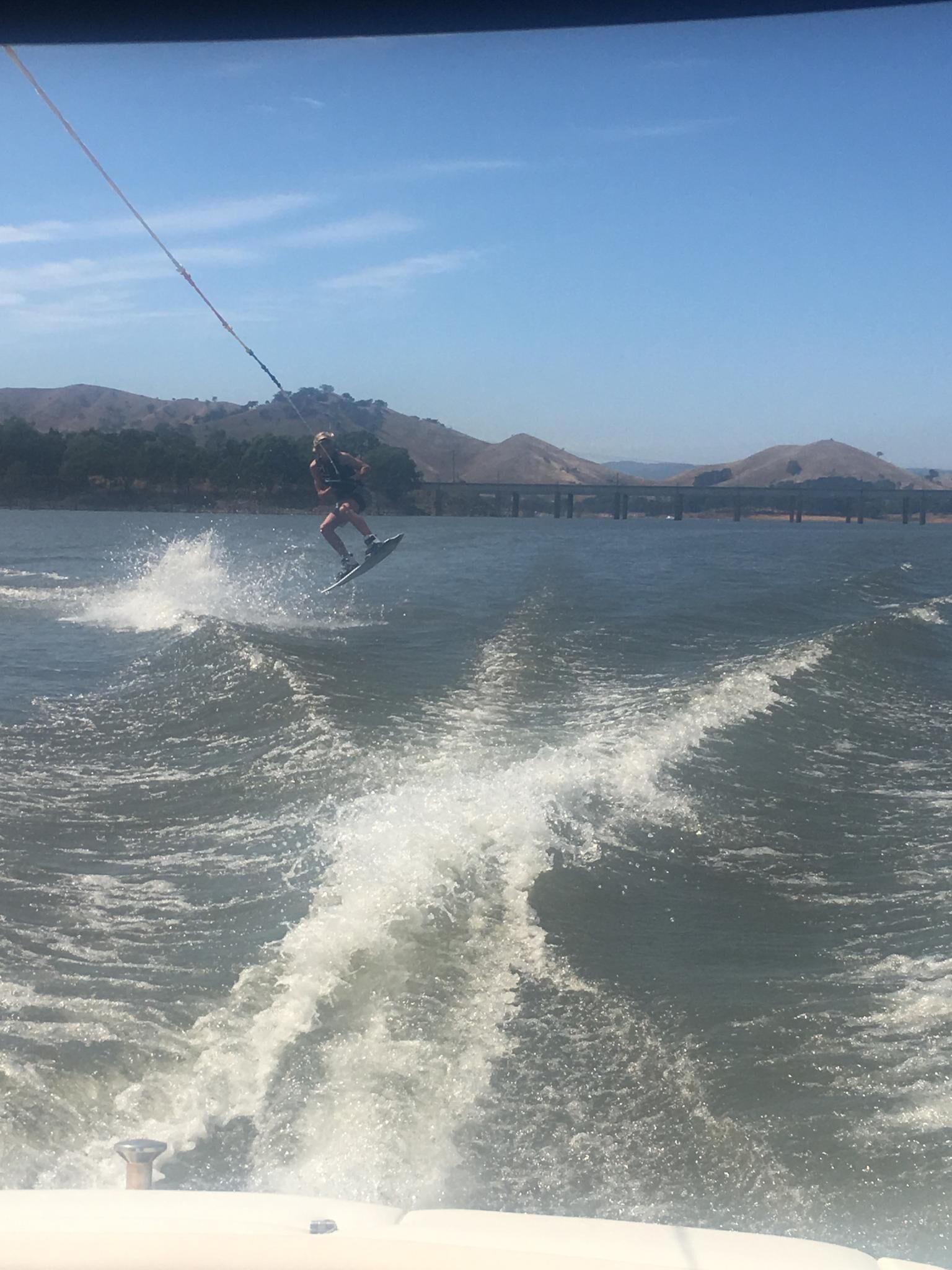 Una persona practica wakeboard en un lago con colinas al fondo.