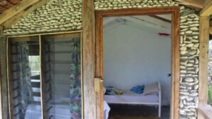 A rustic wooden structure with a stone wall and a glass door leading to a room with a bed and a window. - Tanna Ikamir Bungalows and Accomodations (Tanna Island)