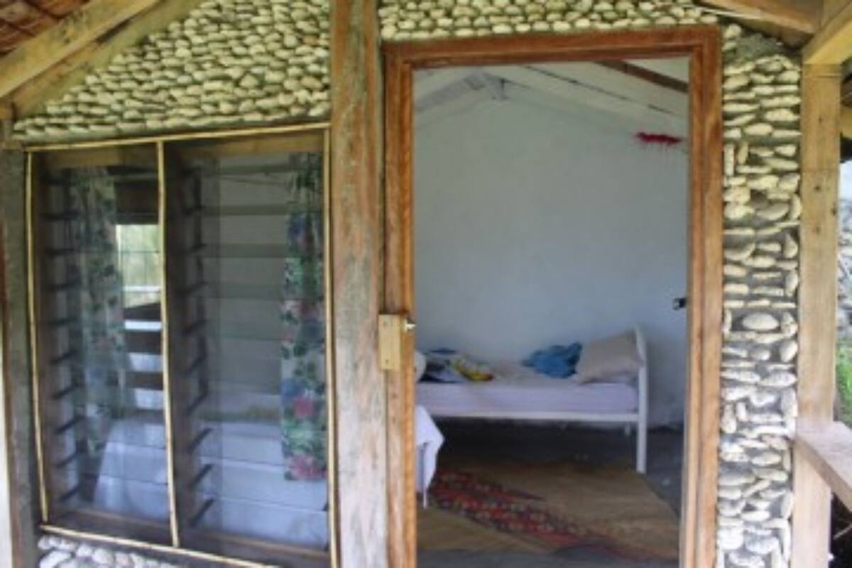 Una estructura rústica de madera con un muro de piedra y un cristal que da a una habitación con cama y ventana.