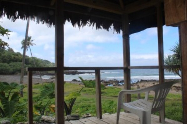 Ein überdachter Außenbereich mit einer Bank, Holzboden und Blick auf Strand und Meer.