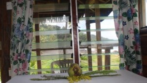 A room with a bed, a window with curtains, and a view of greenery outside. - Tanna Ikamir Bungalows and Accomodations (Tanna Island)