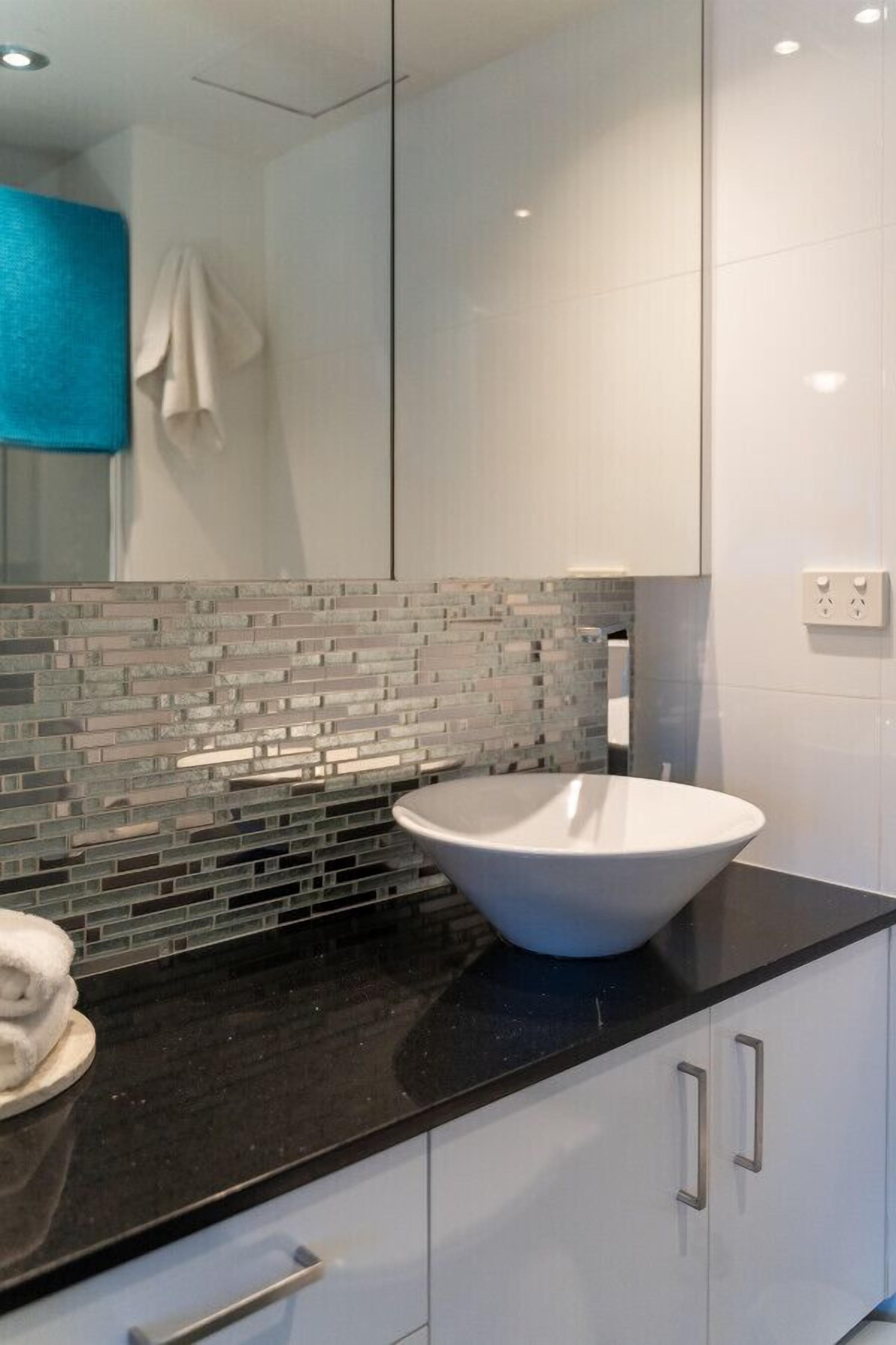 A modern bathroom with a large white sink, a black countertop, and a tiled backsplash.