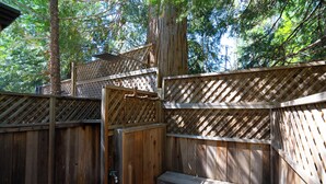 A wooden outdoor deck with a bench and a small table, surrounded by trees.