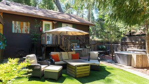 A backyard with a patio, outdoor seating, a hot tub, and a covered area with a staircase leading to a deck.