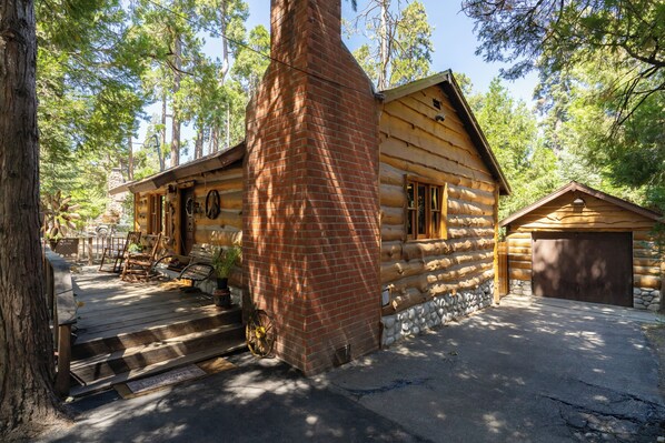 A log cabin with a brick chimney, wooden deck, and a garage. - Arrowhead, A/C, Private Jacuzzi, Huge Backyard, 65" TV, Fully Stocked, Dogs OK. (Twin Peaks)