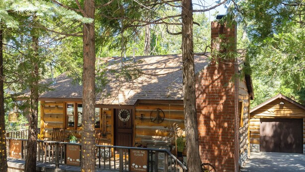 A rustic log cabin with a porch, a wheelbarrow, and a wooden fence.