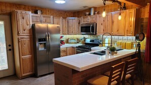 A kitchen with wooden cabinets, stainless steel appliances, a brick island, and a hanging light fixture.