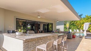 Ein moderner Außenküchenbereich mit einer Steintheke, Barhocker und einer Sitzgelegenheit am Pool.