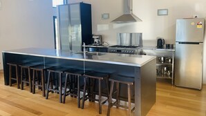 A modern kitchen with a large island, stainless steel appliances, and bar stools. - Modern Beach-House Gem (Dodges Ferry)
