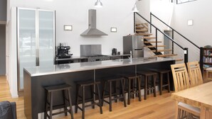 A modern kitchen with a central island, bar stools, and a staircase leading to an upper level. - Modern Beach-House Gem (Dodges Ferry)