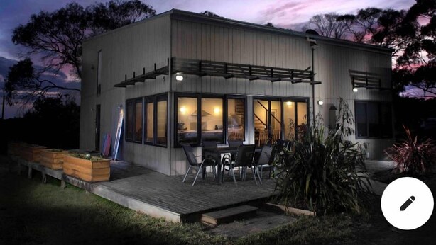 A modern two-story building with a covered patio area, large windows, and a deck with outdoor seating. - Modern Beach-House Gem (Dodges Ferry)