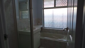 A bathroom with a bathtub, a sink, and a window with a view of a body of water. - OURZ - Close to the beach (Middleton Beach)