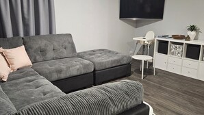 Ein modernes Wohnzimmer mit einer Eckcouch, einem Flachbildfernseher und einer weißen Unterhaltungsanlage.