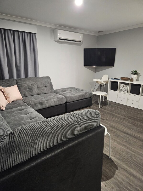 A modern living room with a sectional sofa, a flat-screen TV, and a white entertainment unit. - OURZ - Close to the beach (Middleton Beach)