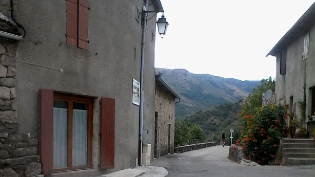A narrow street with stone buildings, a street lamp, and a mountain in the background. - SUNNY HOUSE, LAND RAISED (Aubenas)