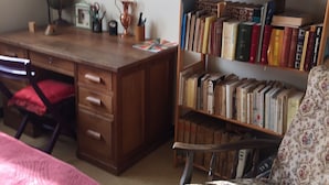 A study room with a wooden desk, a bookshelf, a red chair, and a bed with a red blanket. - SUNNY HOUSE, LAND RAISED (Aubenas)