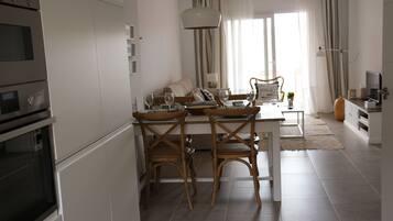 Een moderne keuken met witte kastjes, een eethoek met houten stoelen en een groot raam met gordijnen.
