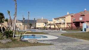 Zona residencial con piscina, palmeras y casas con techos de tejas.