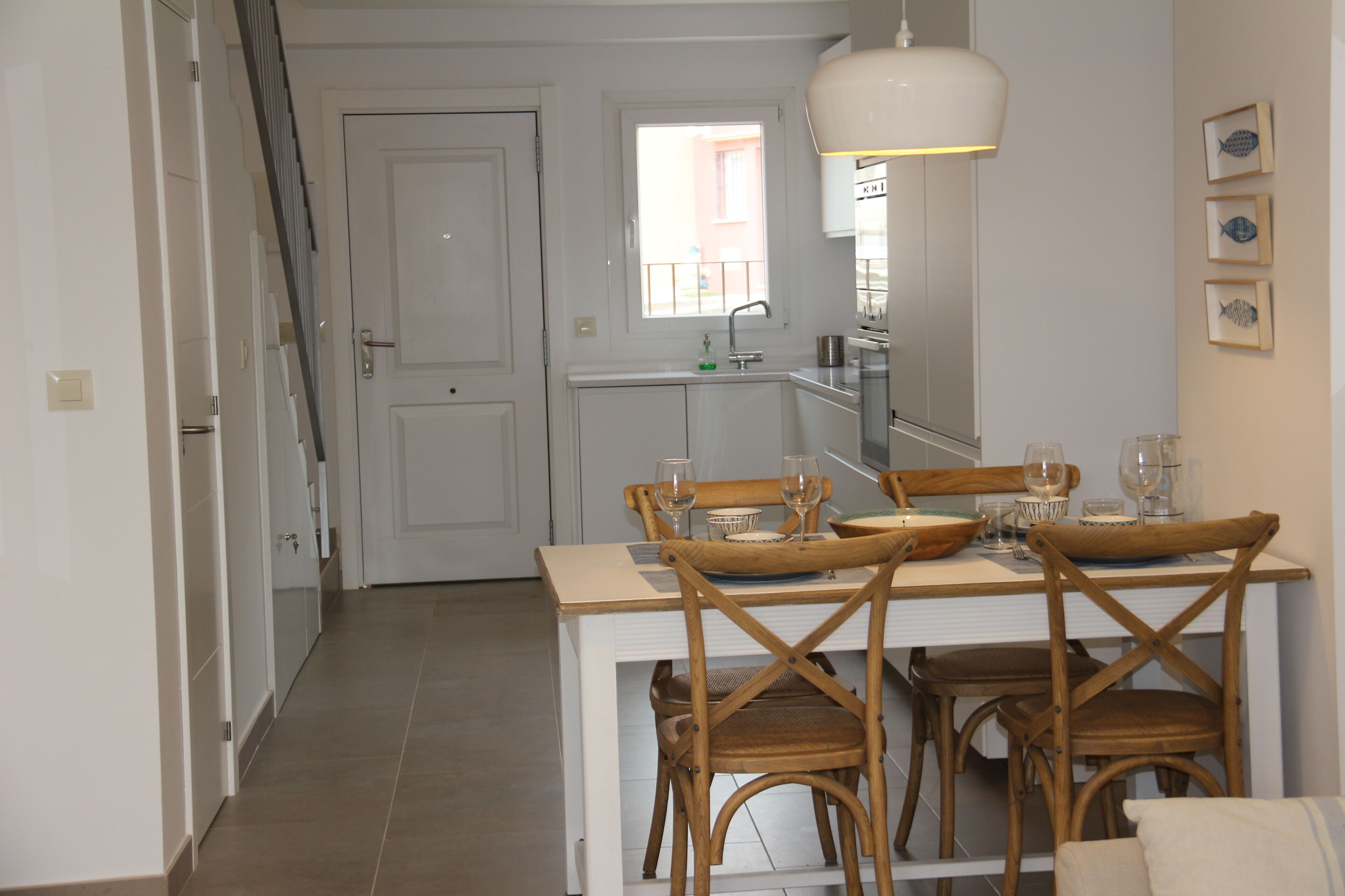 A dining area with a white table, four wooden chairs, and a hanging light fixture.