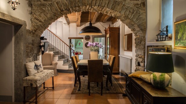 Un espace repas agrémenté d’une arche en pierre, d’une table à manger en bois, de chaises et d’un lustre.