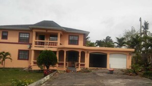 A two-story house with a garage, a covered porch, and a small front yard with plants. - Large home for retreat and family vacation (Mandeville)