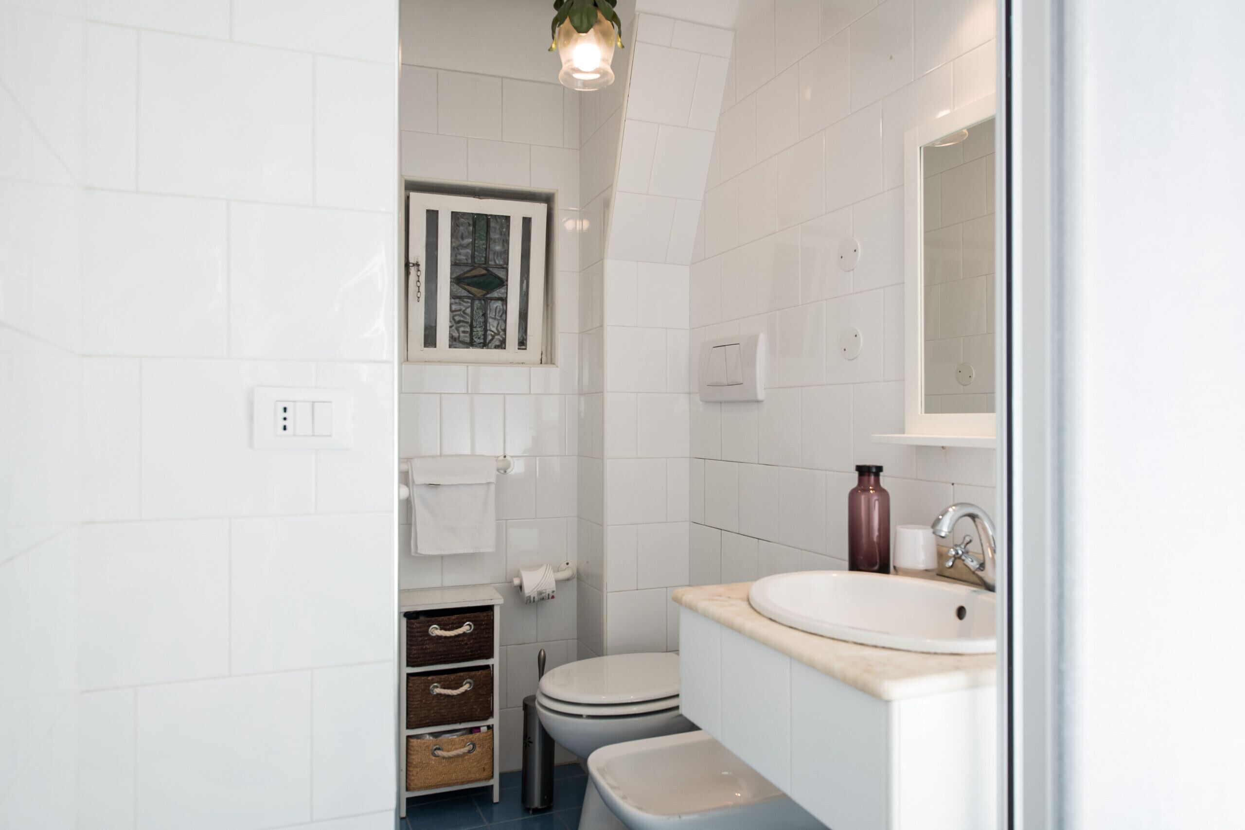 Een moderne badkamer met witte tegels, een toilet, een wastafel en een raam.