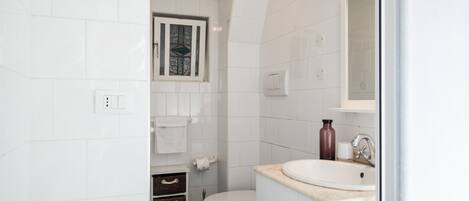 Een moderne badkamer met witte tegels, een toilet, een wastafel en een raam.