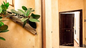 Un pasillo con un estante de madera con plantas verdes, una puerta con picaporte de latón y una pared con textura.