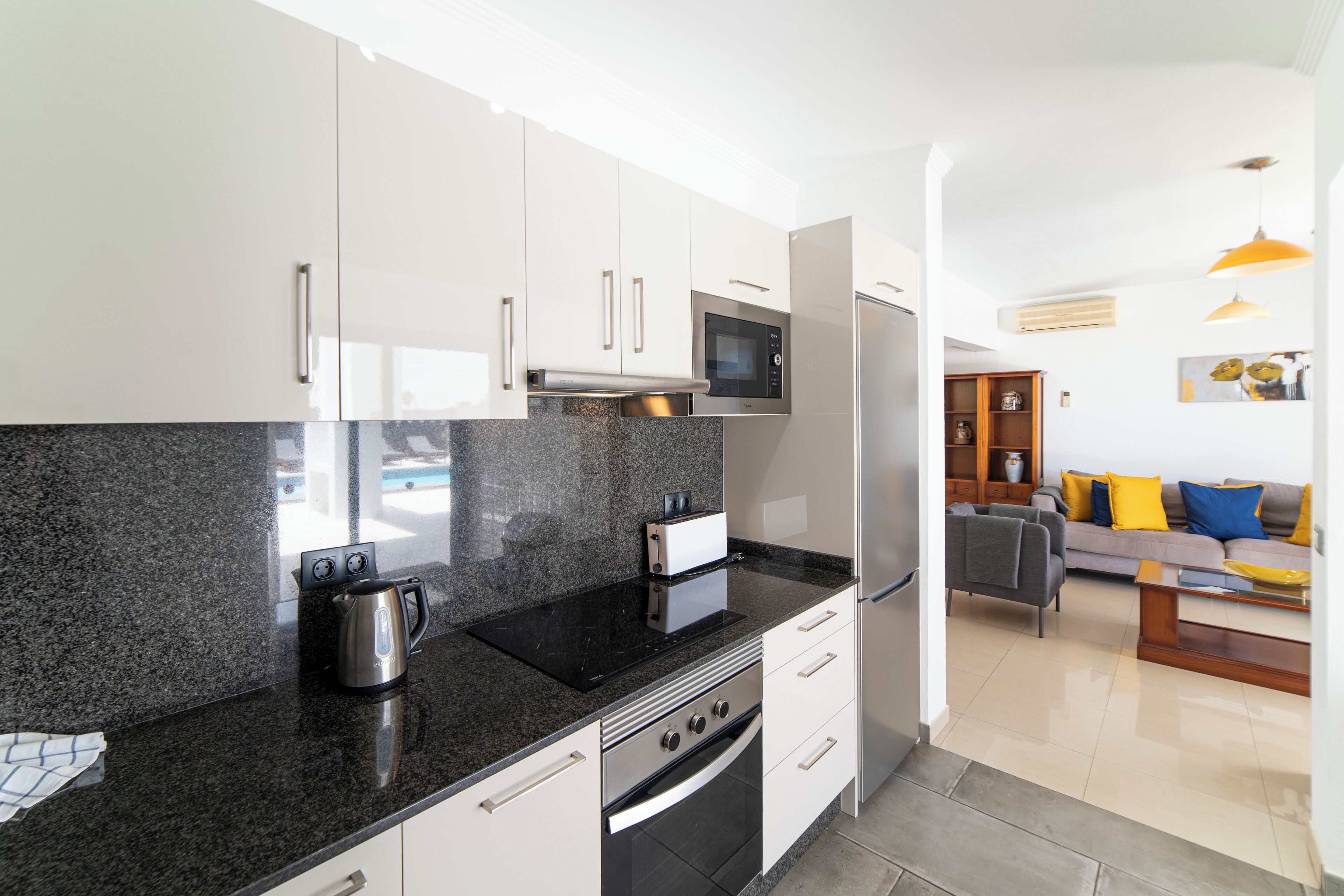 Uma cozinha moderna com armários brancos, bancada preta e eletrodomésticos de aço inoxidável, incluindo micro-ondas, forno e geladeira.