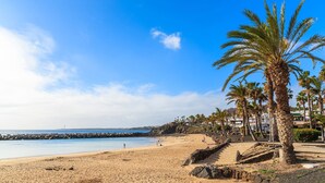 A sandy beach with palm trees and a rocky breakwater. - 3 Bedroom, 3 Bathroom Villa, with Private Pool, WIFI, Playa Blanca, Lanzarote (Playa Blanca)