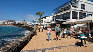 A coastal promenade with a stone wall, outdoor seating, and buildings with signage for restaurants and a hotel. - 3 Bedroom, 3 Bathroom Villa, with Private Pool, WIFI, Playa Blanca, Lanzarote (Playa Blanca)