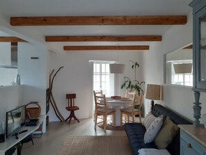 Amplia sala de estar con un sofá de color oscuro, una mesa de comedor con sillas, una lámpara y un ventanal que proporciona luz natural.