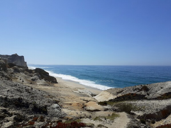 A coastal landscape with rocky terrain and a beach leading to the ocean.