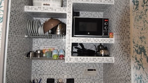Eine kleine Küche mit Spüle, Mikrowelle und verschiedenen Küchenutensilien auf Regalen.