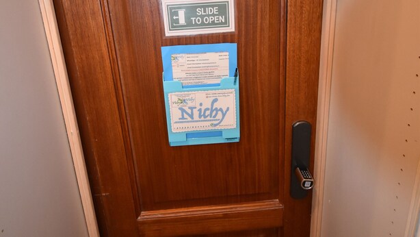 Eine Holztür mit einer Namensschild, auf dem "Nichy" steht, und einem Schild, das anzeigt, dass die Tür geöffnet werden soll.
