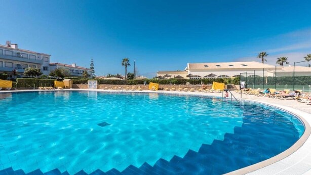 A clear blue swimming pool with steps leading into it, surrounded by sun loungers and palm trees. - Lovely 2 Bedroom Apt on Oasis Parque, Alvor (Portimão)