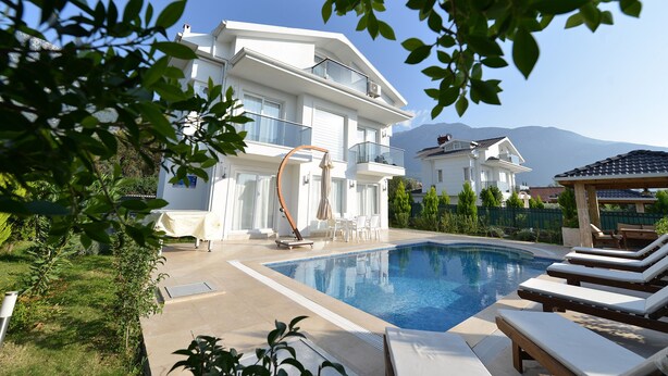 Une maison moderne à deux étages, dotée d’une piscine, d’un espace salon extérieur et offrant une vue sur les montagnes.