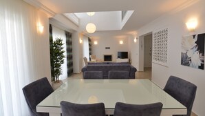 Un salon moderne avec une table à manger en verre, des canapés gris et un téléviseur.