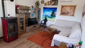 A living room with a sofa, a television, a red heater, and a wooden cabinet. - CASA BOZZERO, elegant and modern rustic with 2 apartments (Krnica)
